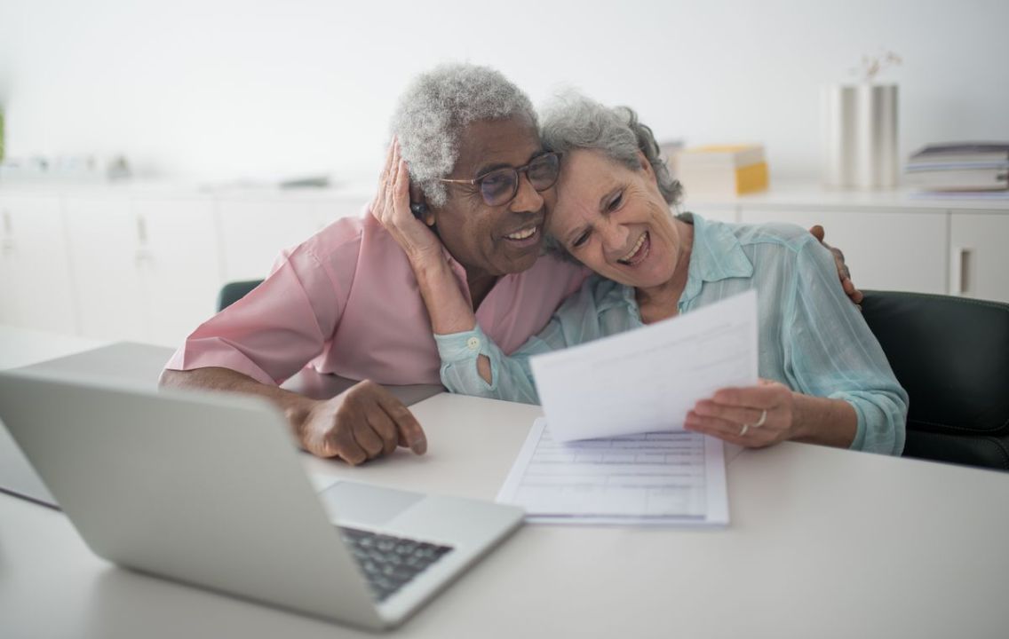 Smiling senior couple reviewing financial documents with a laptop